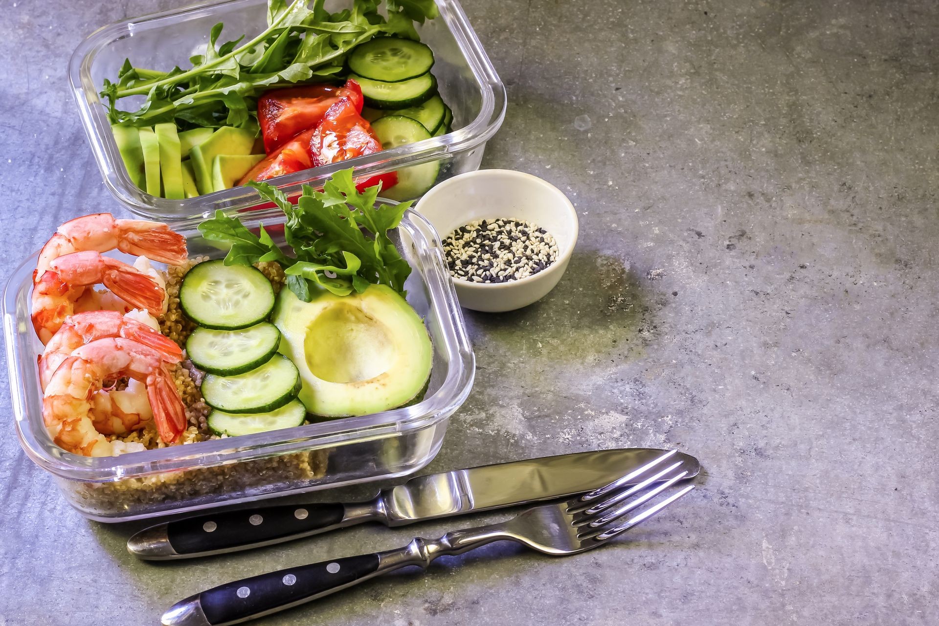 Healthy meal prep containers with quinoa, shrimp, arugula, cucumber and avocado